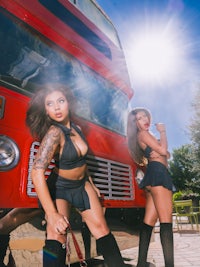 two women posing in front of a red double decker bus