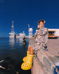 a girl in yellow boots is sitting on a dock talking on a cell phone