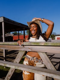 a woman in a cowboy hat leaning on a wooden fence