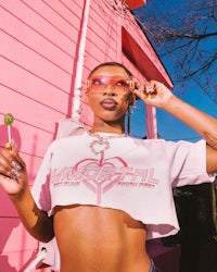 a woman in a pink crop top is posing in front of a pink house