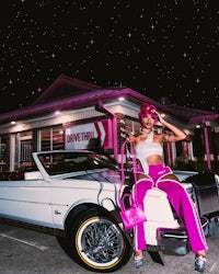 a woman sitting on top of a pink car at night